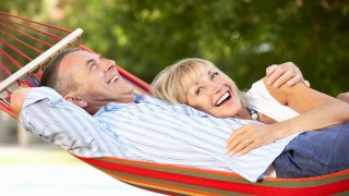 man and women smiling and cuddling together on a hammock outside with green trees in the background