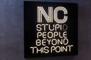 neon style sign on wall with words no stupid people beyond this point