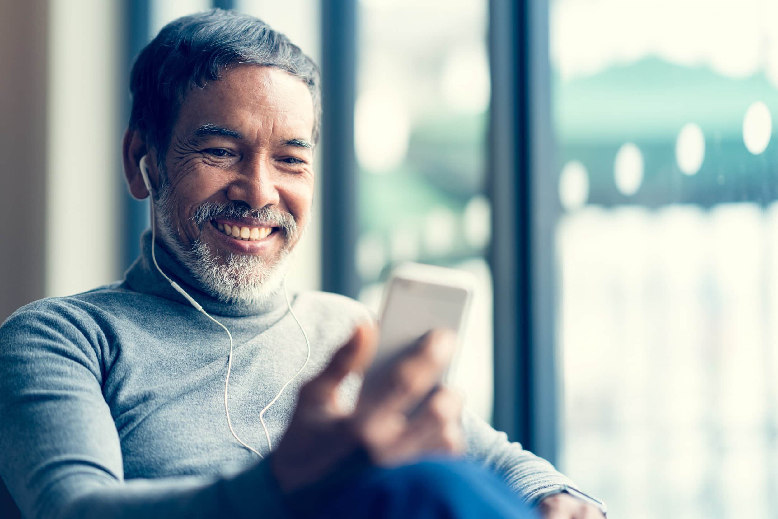 older man wearing earbuds listening to music on his cell phone