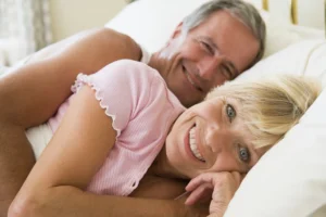 A loving elderly couple cuddling on a bed, using pillows for arthritis-friendly intimacy.
